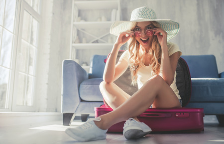 Attractive young woman is preparing for traveling at home while packing suitcaseの写真素材
