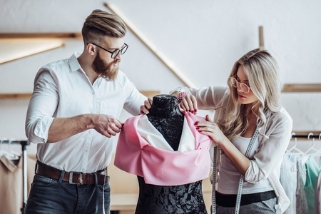 Couple of fashion designers are working in workshop. Attractive young woman and stylish bearded man are in process of creating new clothes collection.の写真素材