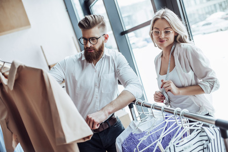 Couple of fashion designers are working in workshop. Attractive young woman and stylish bearded man are in process of creating new clothes collection.の写真素材