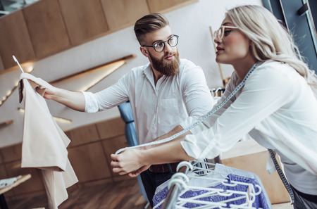 Couple of fashion designers are working in workshop. Attractive young woman and stylish bearded man are in process of creating new clothes collection.の写真素材