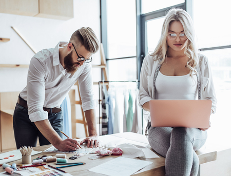 Couple of fashion designers are working in workshop. Attractive young woman and stylish bearded man are in process of creating new clothes collection.の写真素材