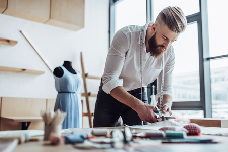 Handsome male fashion designer is working in his workshop. Stylish bearded man in process of creating new clothes collection.の写真素材
