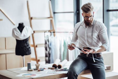 Handsome male fashion designer is working in his workshop. Stylish bearded man in process of creating new clothes collection.の写真素材