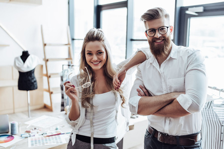Couple of fashion designers are working in workshop. Attractive young woman and stylish bearded man are in process of creating new clothes collection.の写真素材