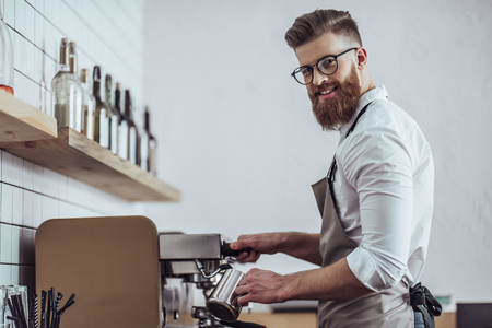 Handsome male barista is working in coffee shop. Bearded man behind the bar counter is making coffee.の写真素材