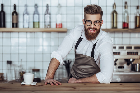 Handsome male barista is working in coffee shop. Bearded man behind the bar counter is making coffee.の写真素材