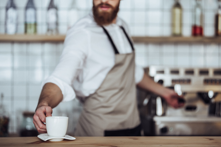 Cropped image of handsome male barista is working in coffee shop. Bearded man behind the bar counter is making coffee.の写真素材
