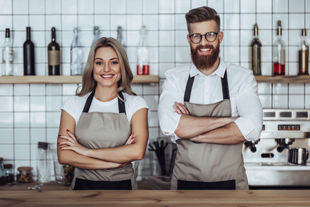 Couple of barista are working in coffee shop. Attractive young woman and handsome bearded man are standing together behind the bar counterの写真素材