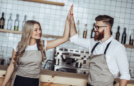 Couple of barista are working in coffee shop. Attractive young woman and handsome bearded man are standing together behind the bar counterの写真素材