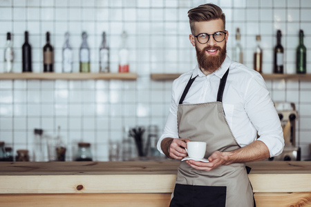 Handsome male barista is working in coffee shop. Bearded man behind the bar counter is making coffee.の写真素材