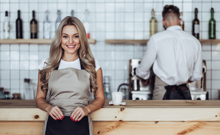 Couple of barista are working in coffee shop. Attractive young woman and handsome bearded man are standing together behind the bar counterの写真素材