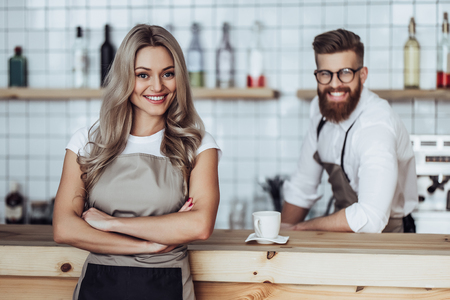 Couple of barista are working in coffee shop. Attractive young woman and handsome bearded man are standing together behind the bar counterの写真素材