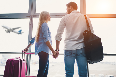 Romantic couple in airport. Attractive young woman and handsome man with suitcases are ready for traveling. Standing near panoramic windows while waiting for departure.の写真素材