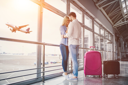 Romantic couple in airport. Attractive young woman and handsome man with suitcases are ready for traveling. Standing near panoramic windows while waiting for departure.の写真素材