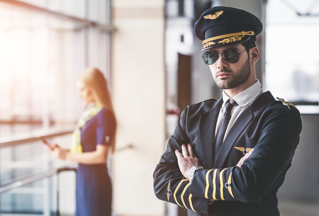 Handsome male pilot and attractive female flight attendant are standing in airport terminal together.の写真素材