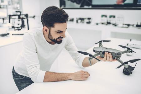 Handsome young man in modern light quadcopter store. Choosing the appropriate droneの写真素材