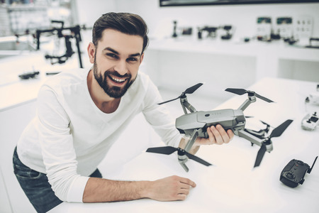 Handsome young man in modern light quadcopter store. Choosing the appropriate droneの写真素材