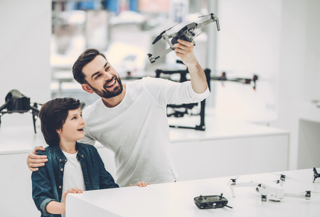 Handsome young man and his cute son are in modern light quadcopter store. Choosing the appropriate...