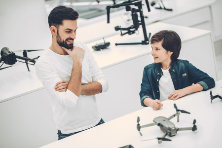 Handsome young man and his cute son are in modern light quadcopter store. Choosing the appropriate droneの写真素材