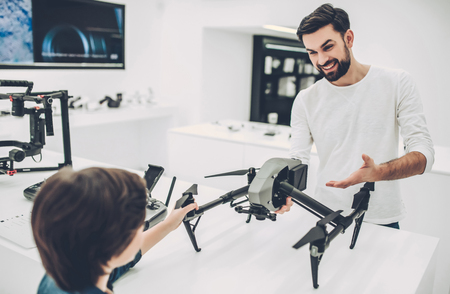 Handsome young man and his cute son are in modern light quadcopter store. Choosing the appropriate droneの写真素材