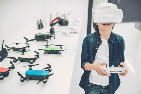 Cute little boy in modern light quadcopter store is standing wearing glasses of virtual reality.の写真素材