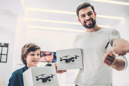 Handsome young man and his cute son are in modern light quadcopter store. Choosing the appropriate droneの写真素材