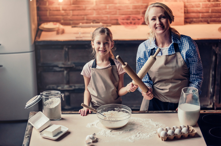 Grandmother and granddaughter are cooking on kitchen. Making tasty baking together. Having fun with rolling pins.の写真素材