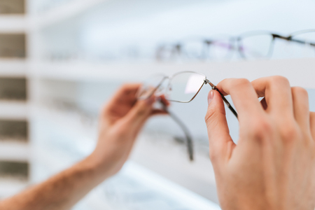 Cropped image of handsome young man is choosing the most appropriate eyeglasses in modern ophthalmology clinic.の写真素材