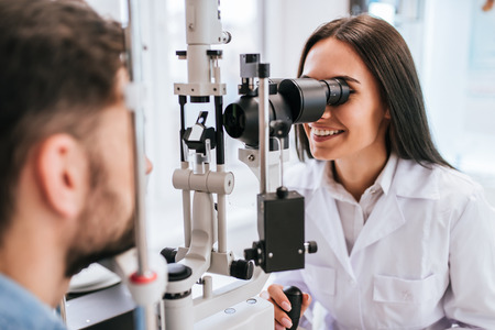 Attractive female doctor  ophthalmologist is checking the eye vision of handsome young man in modern clinic. Doctor and patient in ophthalmology clinic.の写真素材