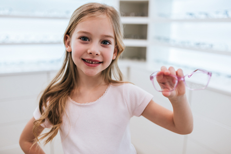 Little cute girl is holding eyeglasses in hands in modern ophthalmology clinic.の写真素材