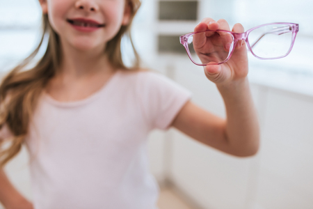 Cropped image of little cute girl is holding eyeglasses in hands in modern ophthalmology clinic.の写真素材