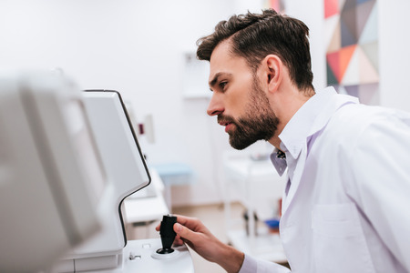 Young handsome male doctor ophthalmologist is working in modern ophthalmology clinic.の写真素材