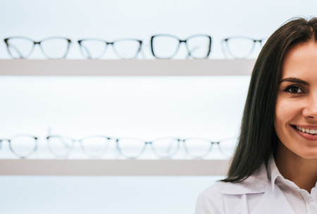 Cropped image of attractive young female doctor in ophthalmology clinic. Doctor ophthalmologist is standing near shelves with different eyeglasses.の写真素材