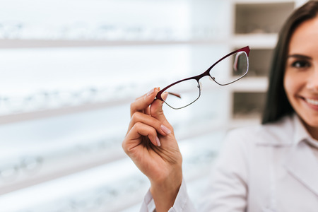 Cropped image of attractive young female doctor in ophthalmology clinic. Doctor ophthalmologist is standing near shelves with different eyeglasses.の写真素材