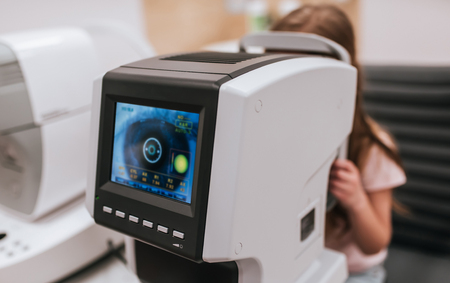 Little cute girl is checking the eye vision in ophthalmology clinic. Tools for checking the eye vision and eye health in modern ophthalmology clinic.の写真素材