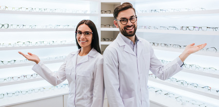 Doctors in ophthalmology clinic. Two ophthalmologists are standing near shelves with big choice of different eye glasses.の写真素材
