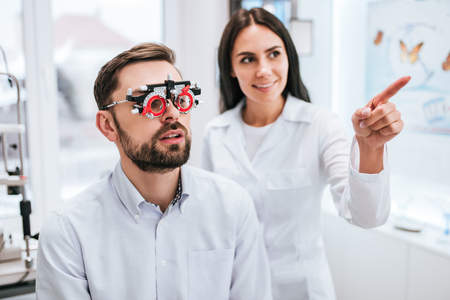 Attractive female doctor  ophthalmologist is checking the eye vision of handsome young man in modern clinic. Doctor and patient in ophthalmology clinic.の写真素材
