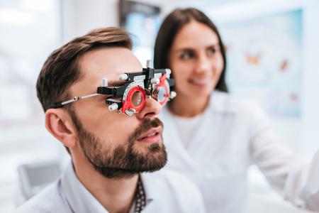 Attractive female doctor  ophthalmologist is checking the eye vision of handsome young man in modern clinic. Doctor and patient in ophthalmology clinic.の写真素材