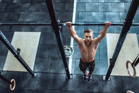 Strong muscular man is working out in gym. Cross fit training. Shirtless man doing pull ups.の写真素材