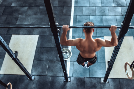 Strong muscular man is working out in gym. Cross fit training. Shirtless man doing pull ups.