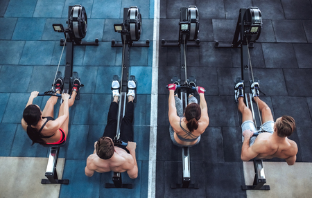 Group of sporty muscular people are working out in gym. Cross fit training. Paddling training apparatus. Top view of four sportsmen are rowing together.の写真素材