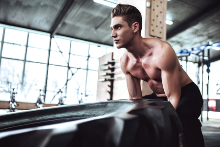 Strong muscular man is working out in gym. Cross fit training. Pushing tire.の写真素材