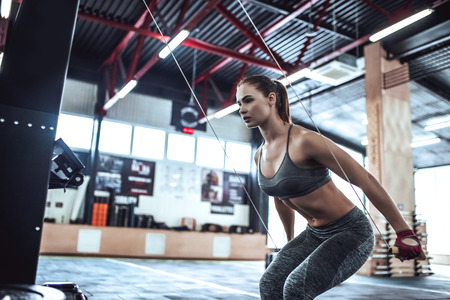 Attractive young sporty woman is working out in gym. Cross fit training. Upper body exercise.の写真素材