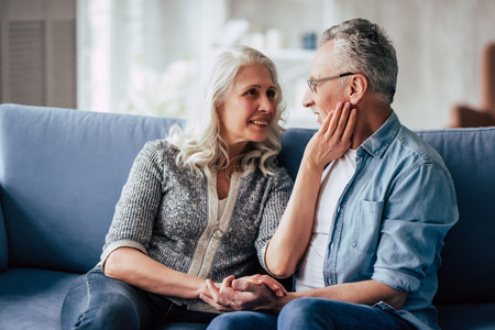 Love lives forever! Senior couple at home. Handsome old man and attractive old woman are spending time together. Sitting on a sofa, hugging and holding hands.の写真素材