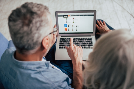 Love lives forever! Senior couple at home. Handsome old man and attractive old woman are spending time together. Sitting on a sofa with laptop.の写真素材