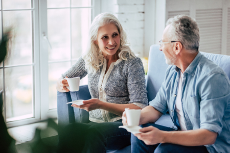 Love lives forever! Senior couple at home. Handsome old man and attractive old woman are spending time together. Drinking tea while sitting on a sofa.の写真素材