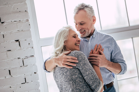 Love lives forever! Senior couple at home. Handsome old man and attractive old woman are hugging and...