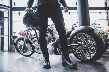 Handsome bearded man in motorcycle shop. Biker is choosing new vehicle and motorcycle accessories. Cropped image of man standing with helmet. Safety driving concept.の写真素材