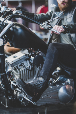 Handsome bearded man in motorcycle shop. Biker is choosing new vehicle and motorcycle accessories. Cropped image of man sitting on bike.の写真素材