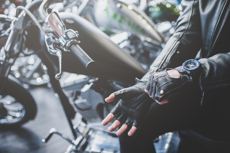 Handsome bearded man in motorcycle shop. Biker is choosing new vehicle and motorcycle accessories. Cropped image of man sitting on bike and wearing gloves.の写真素材